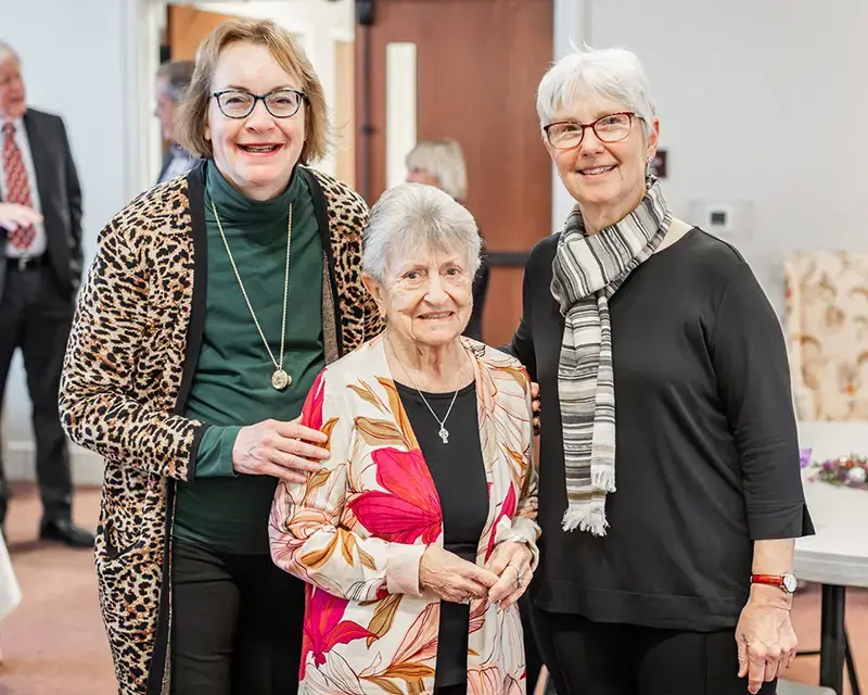 Three women stand together smiling at a church gathering.