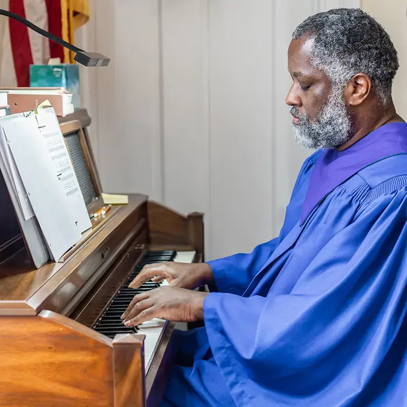 A choir member in a blue robe plays the organ using sheet music.