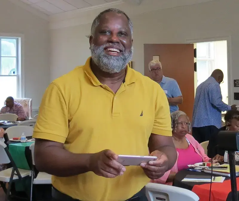 A smiling man holds a tablet during a Bible study gathering in the parish hall