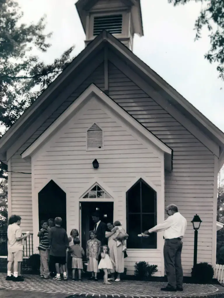 Congregation gathering outside the historic white clapboard chapel with bell tower