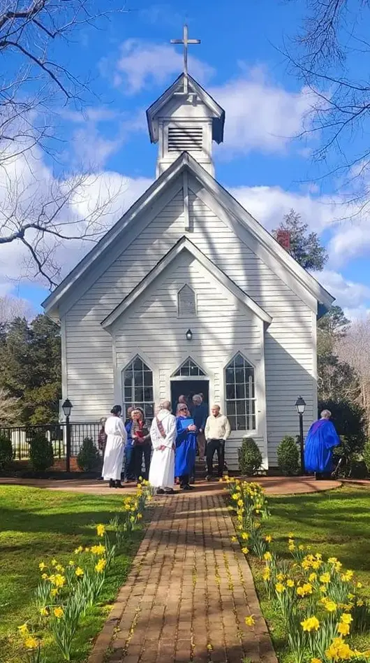 Parishioners gather outside the historic white chapel after Sunday service with spring daffodils in bloom